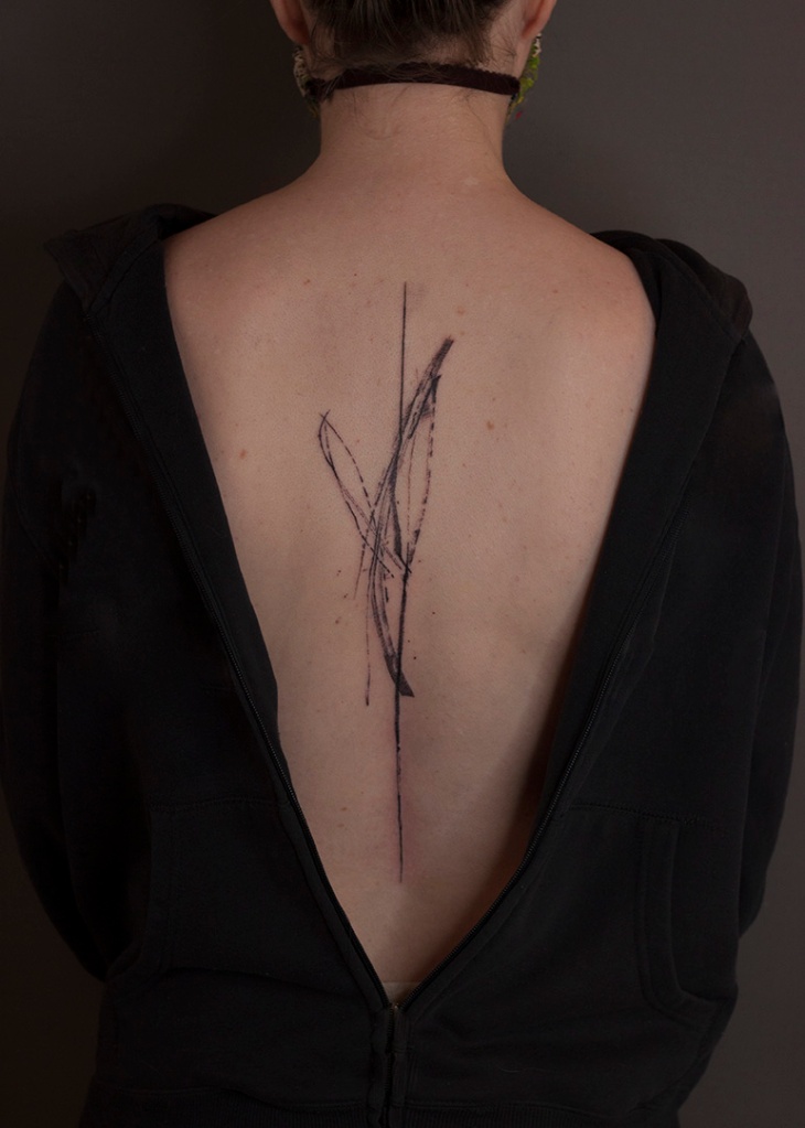 abstracte tattoo op rug tussen de schouderbladen. Lijnen met textuur, alsof het met inkt op het lichaam getekend is